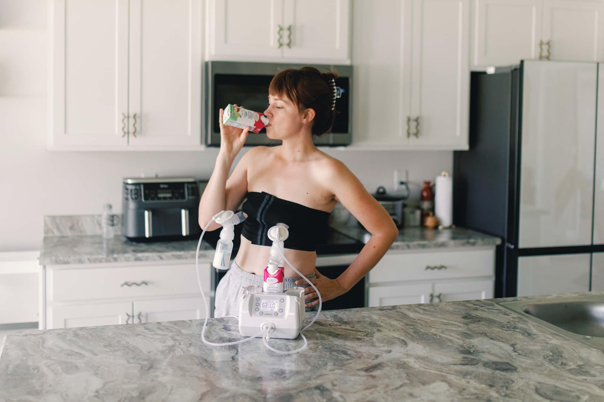 Person drinking lactation smoothie while using breast pump