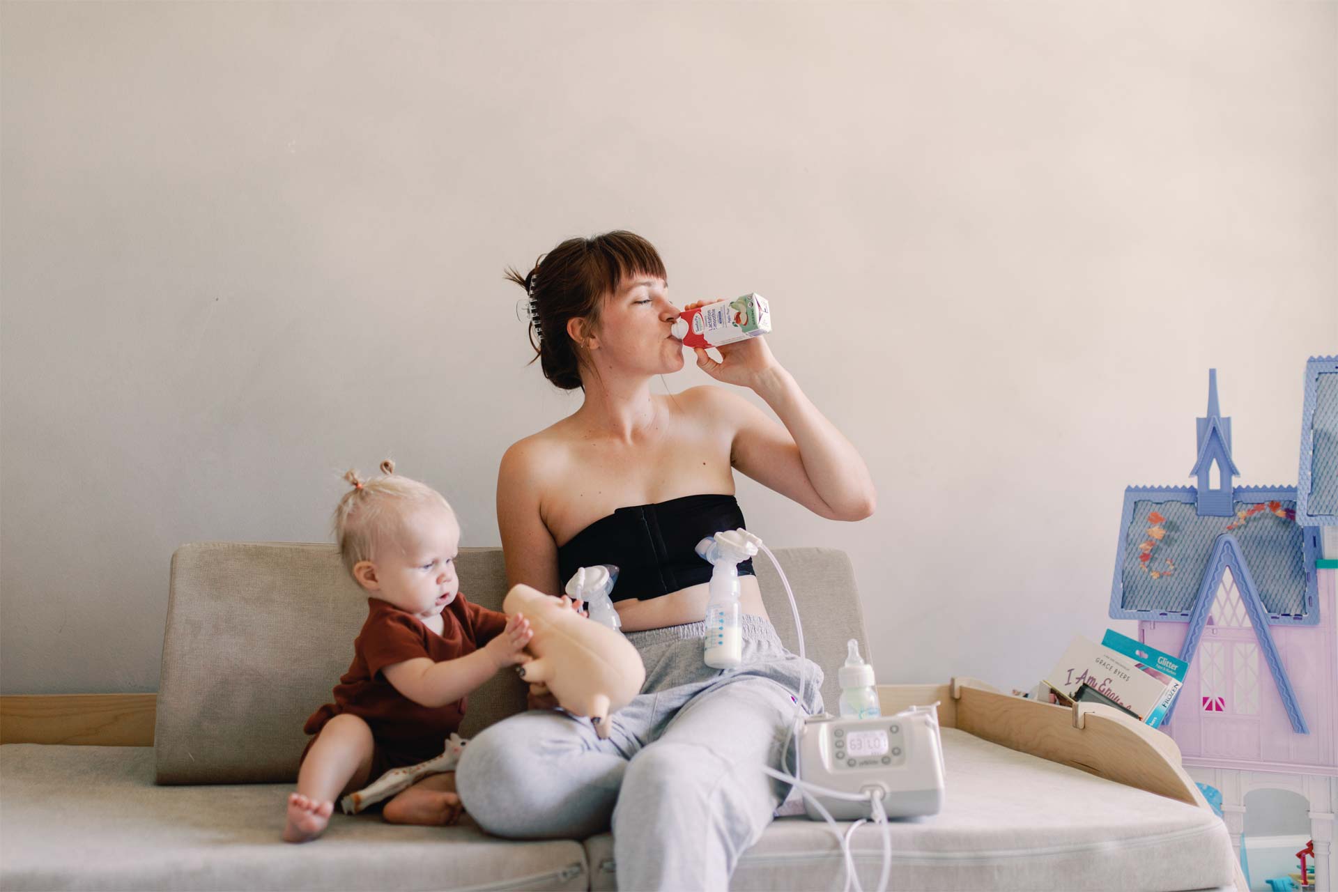 Parent drinking lactation smoothie while pumping next to infant
