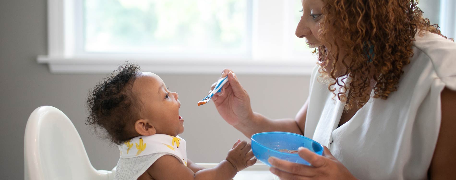 Mother feeding toddler in high chair solid foods