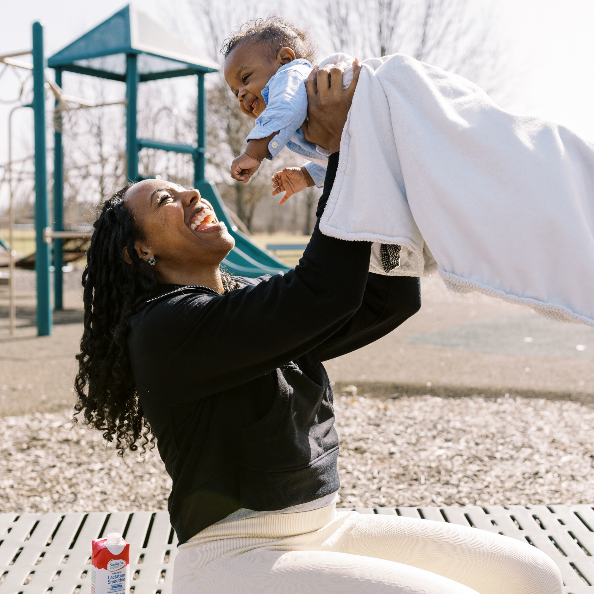 Lifestyle image of mom at the park lifting her young baby up
